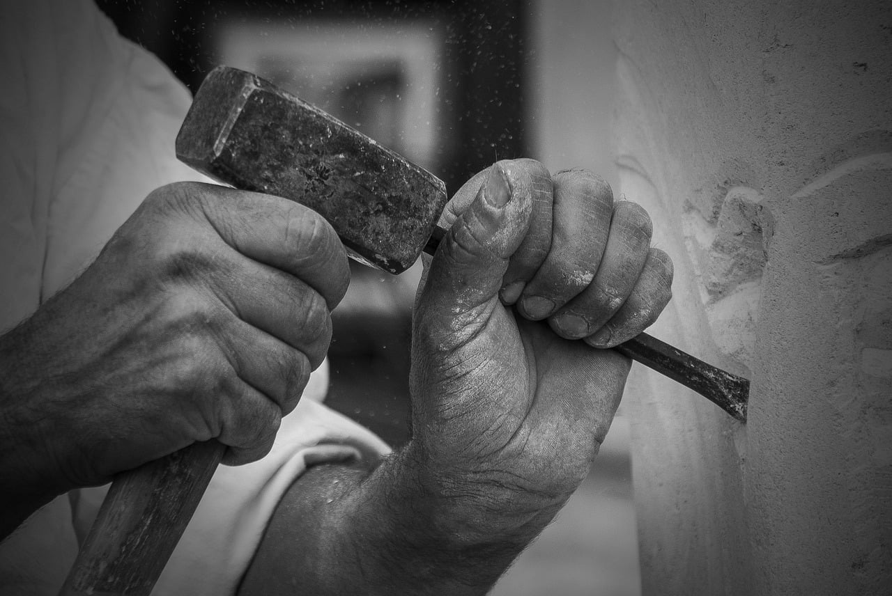 A stone sculptor's skilled hands working with hammer and chisel, embodying Karma Yoga principles from the Bhagavad Gita - action performed with complete dedication yet detachment from ego. This black and white image captures the essence of following one's dharma through disciplined craftsmanship, illustrating how skilled work becomes spiritual practice when performed as sacred offering, a central teaching of the Bhagavad Gita where Krishna instructs Arjuna to fulfill his duty with detached devotion.
