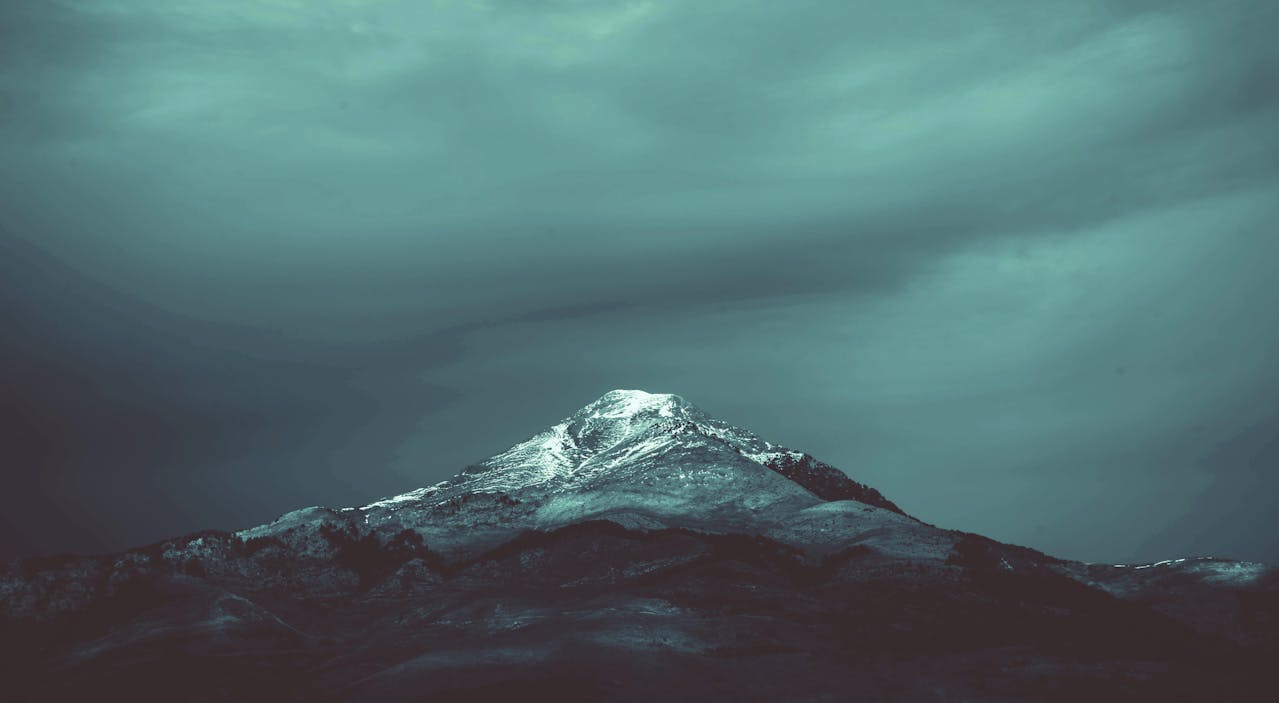 A solitary snow-capped mountain peak illuminated against a dark, moody sky - symbolizing the spiritual journey and different levels of enlightenment.
