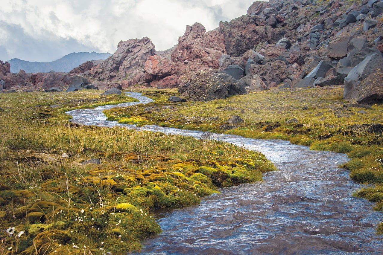 A winding stream embodying Wu Wei as it flows naturally along the path of least resistance through rugged volcanic terrain, demonstrating the Taoist principle of water's effortless strength.